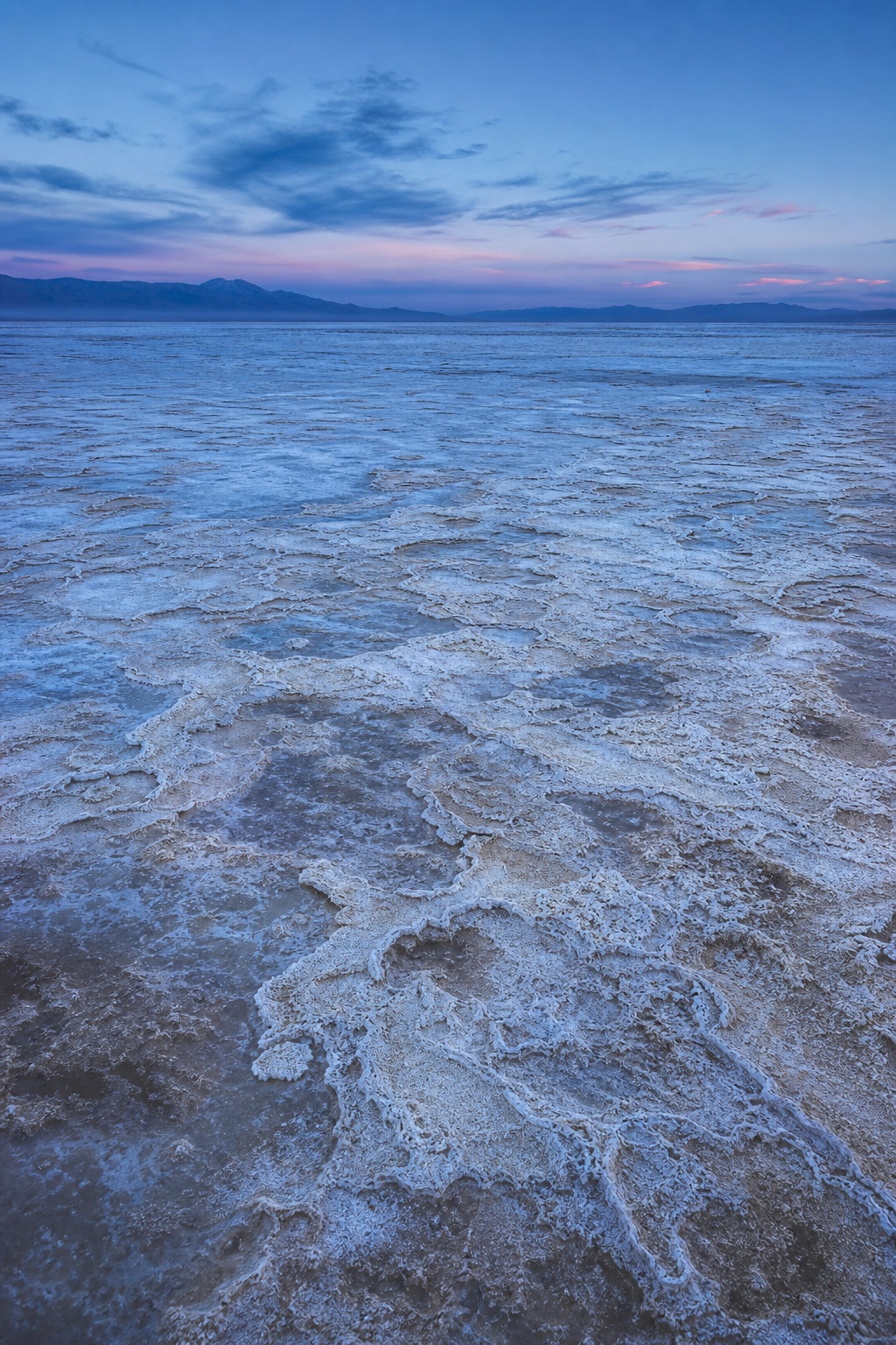 Blue twilight over a salt flat with weathered mineral crust and distant mountains
