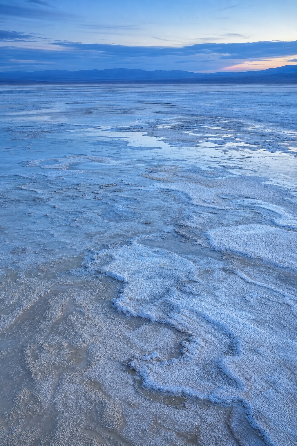 Blue twilight over a salt flat with pale clay patterns and distant horizon