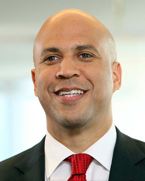 Smiling bald businessman in a black suit and red tie against a soft light background.