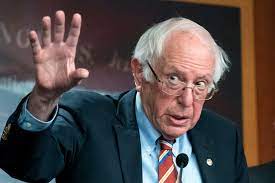 Bernie Sanders speaking and raising one hand during a public appearance.