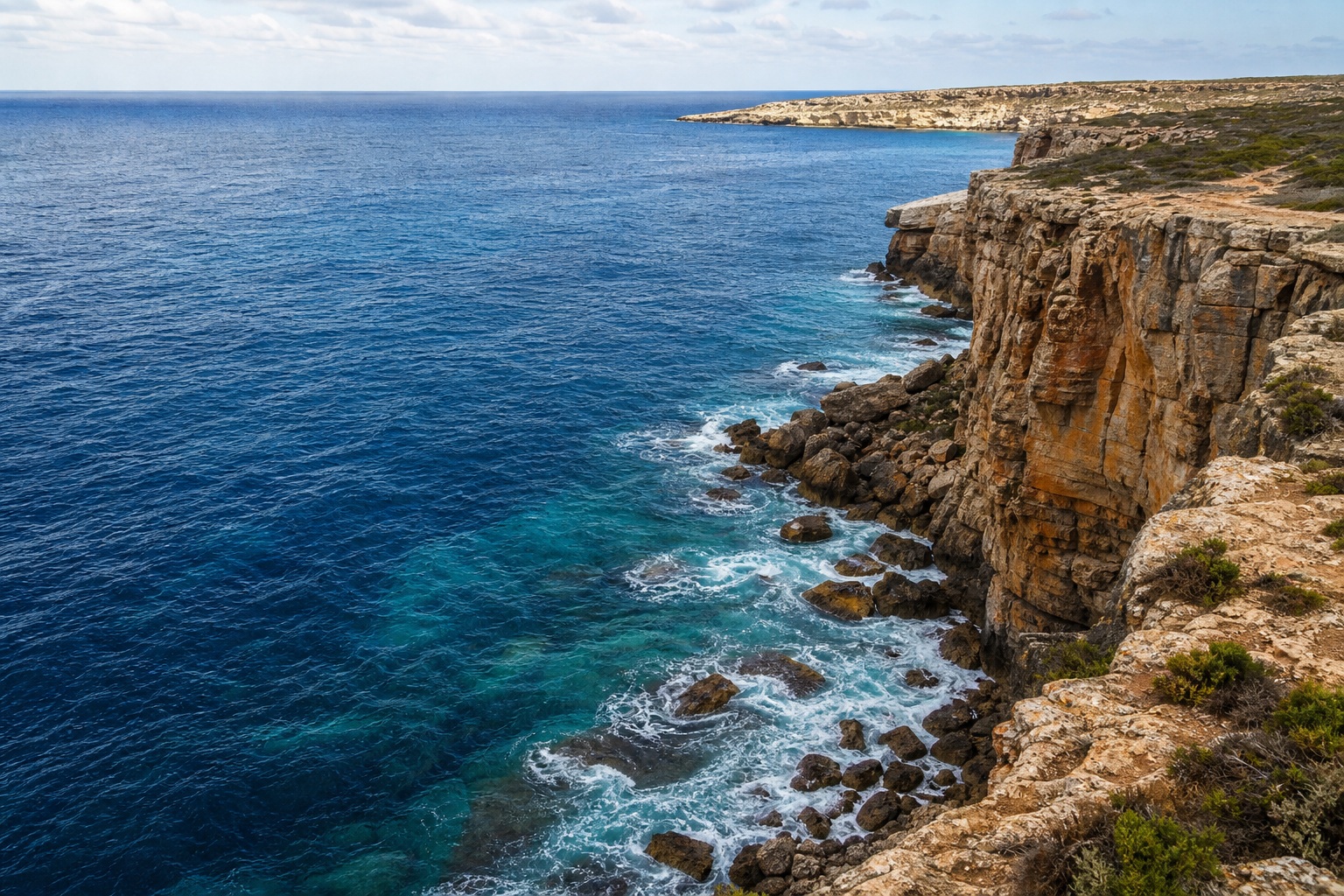 Rocky coastal cliffs overlooking deep blue ocean with waves below