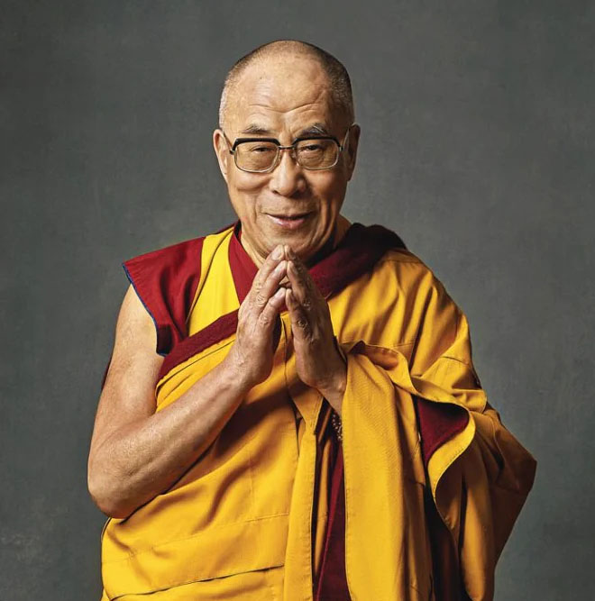 Dalai Lama standing with hands together in a meditation pose against a dark background.