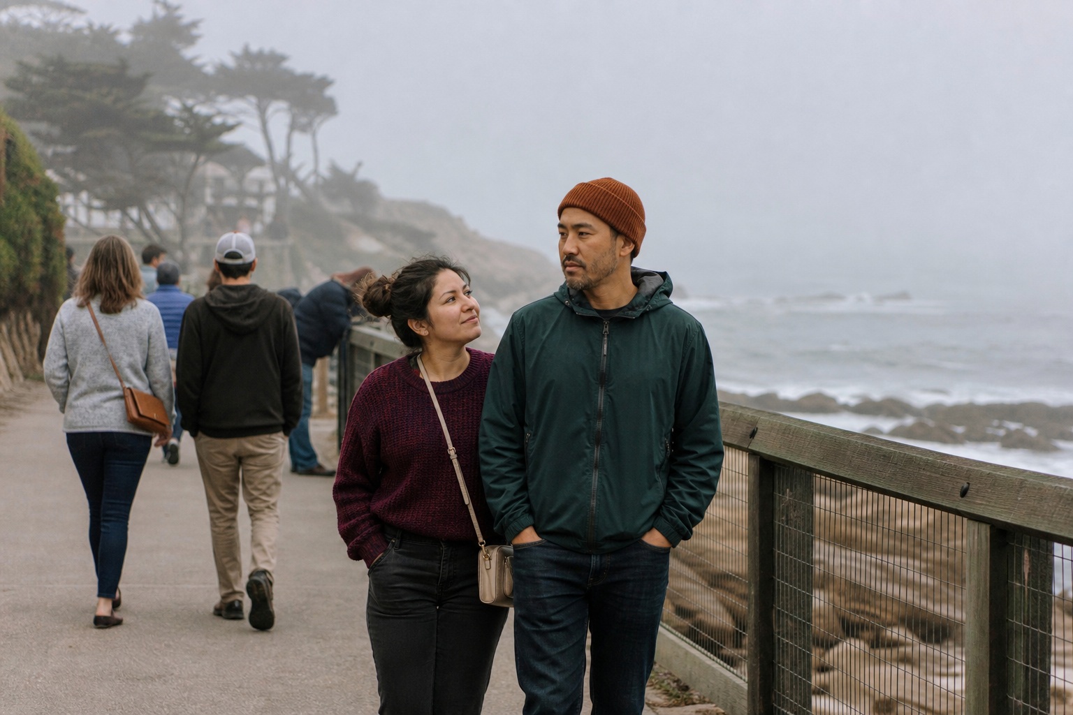 People walking along a foggy coastal boardwalk beside the water