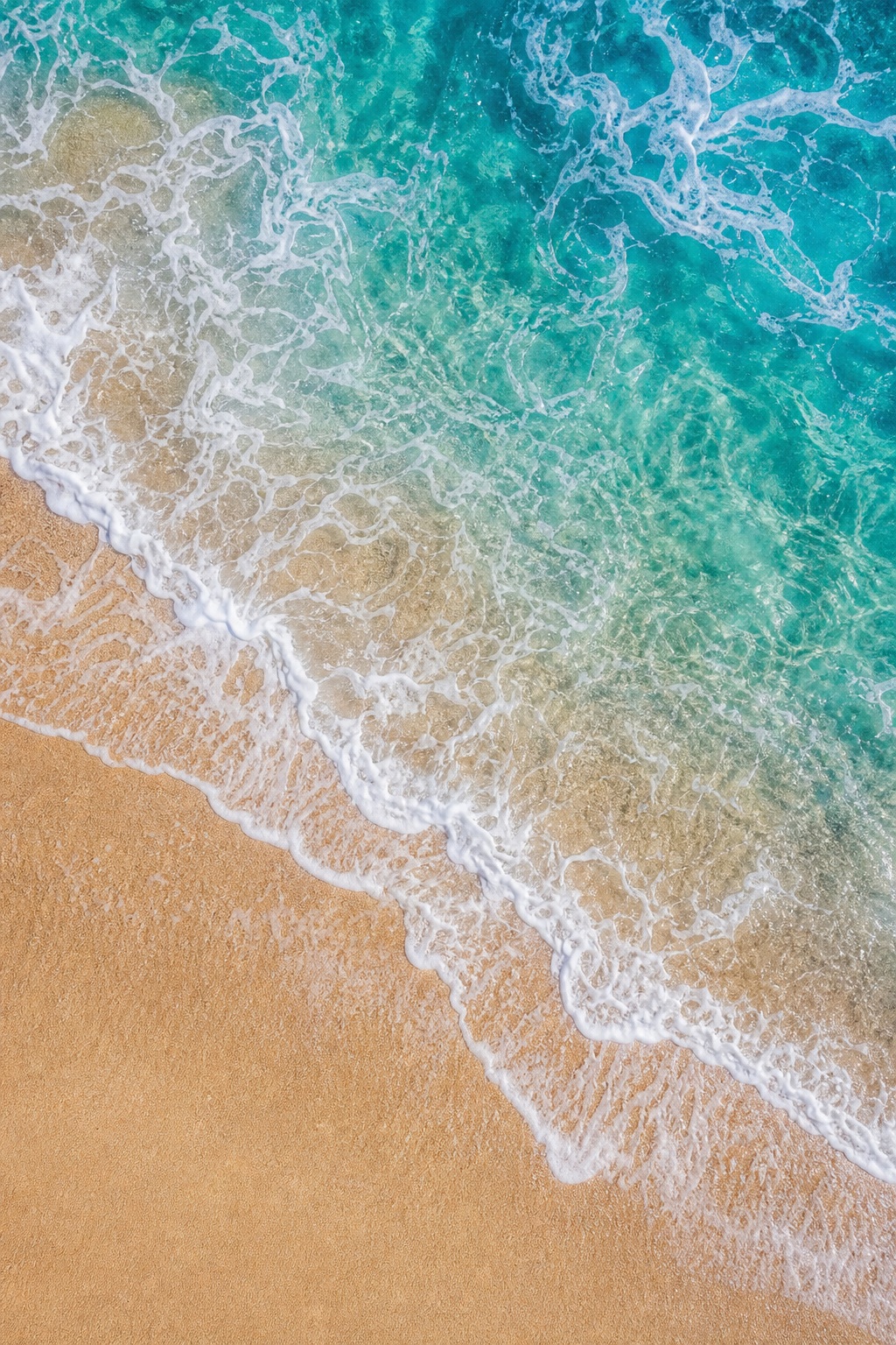 Top-down view of turquoise ocean waves washing over wet sandy shoreline