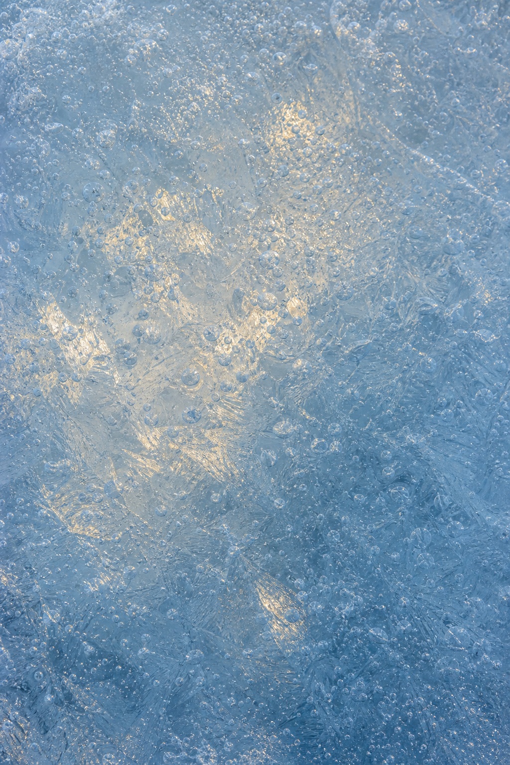 Blue frosted ice surface with cloudy trapped air layers and soft warm highlights
