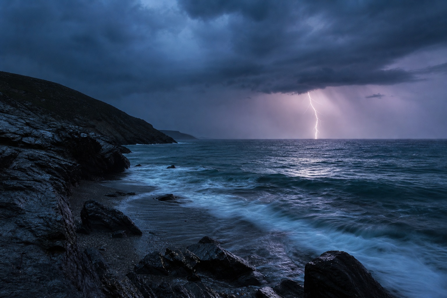 Lightning strikes over a dark stormy ocean beside rocky coastline at dusk.