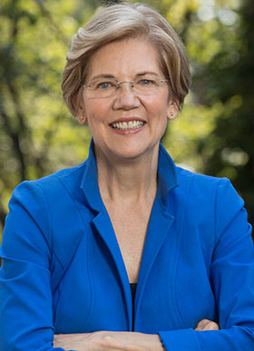 Smiling woman in a blue blazer standing with arms crossed against a blurred outdoor background.