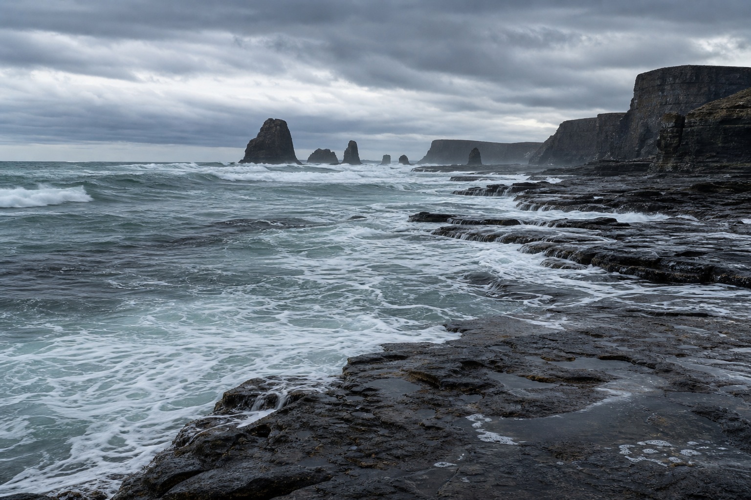 Stormy ocean waves around sea stacks and a dark rocky coastal shelf.