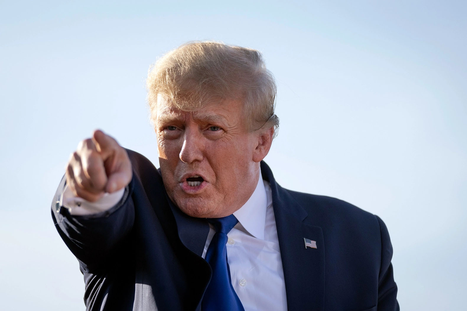 Donald Trump pointing a finger forward against a light blue background.