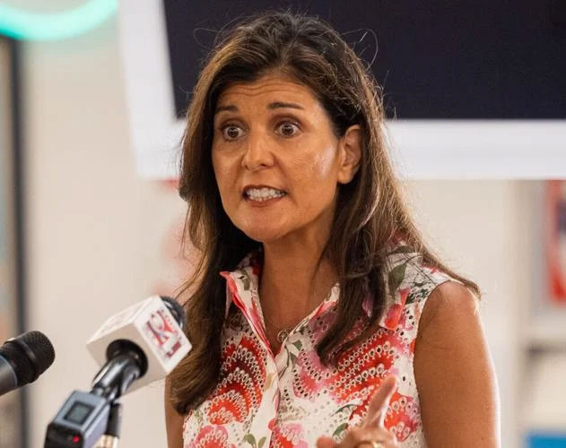 Woman speaking at a press conference with microphones in front of her