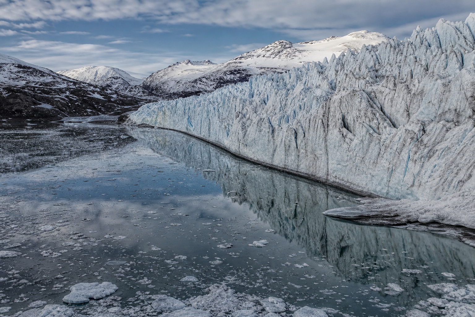 Blue glacier tongue reflecting in calm polar water beside icy shoreline