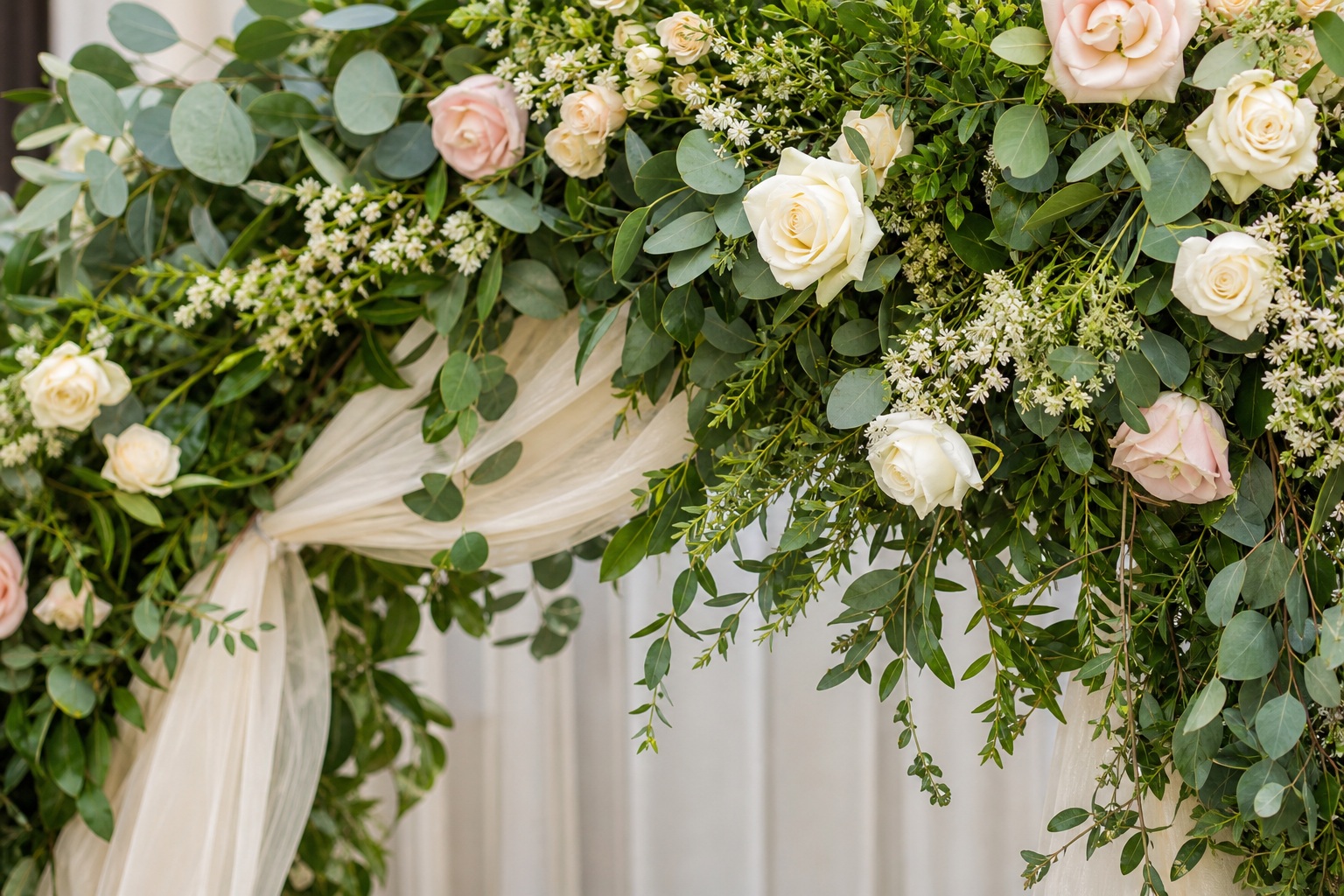 Soft wedding floral arch with greenery, cream drapery, and blush roses
