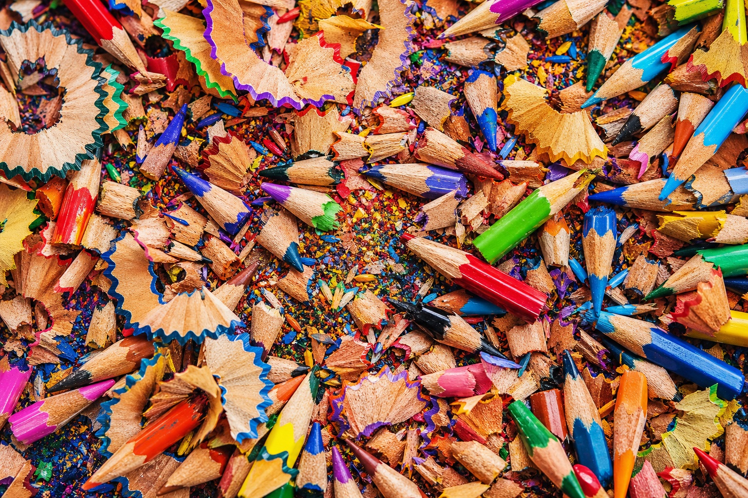 Colorful pencil shavings scattered around sharpened colored pencil tips.