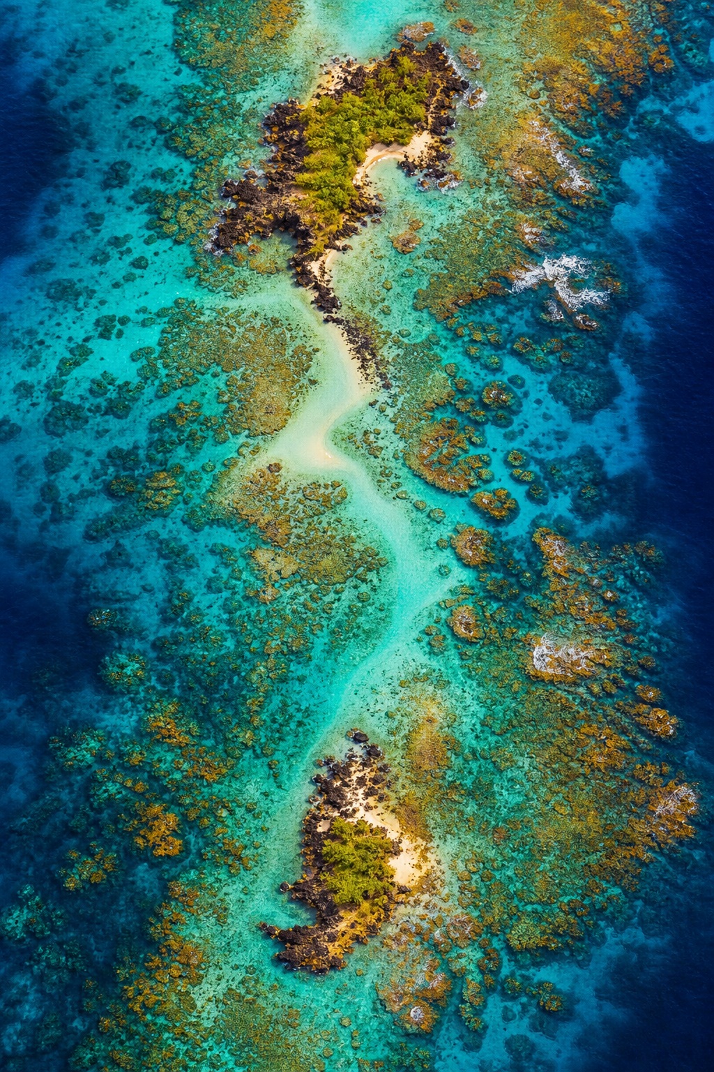 Aerial view of turquoise ocean water with coral formations and a narrow sandy channel