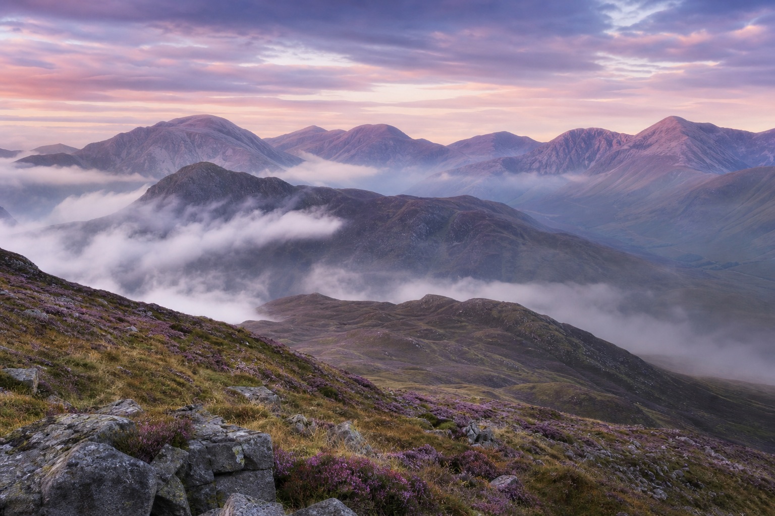 Pastel mist rising over layered mountains and rocky highland slopes at sunrise