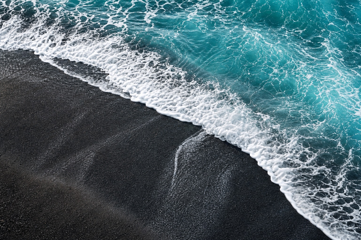 Aquamarine waves washing over black sand with white sea foam at the shoreline.