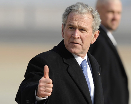 George W. Bush in a suit giving a thumbs up outdoors with a blurred background