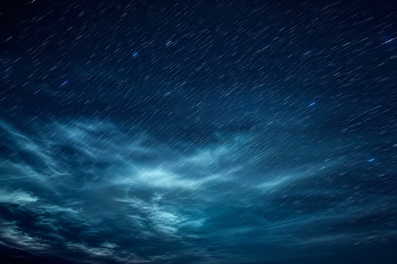 Navy cyan night sky with long exposure star trails and wispy cloud streaks.