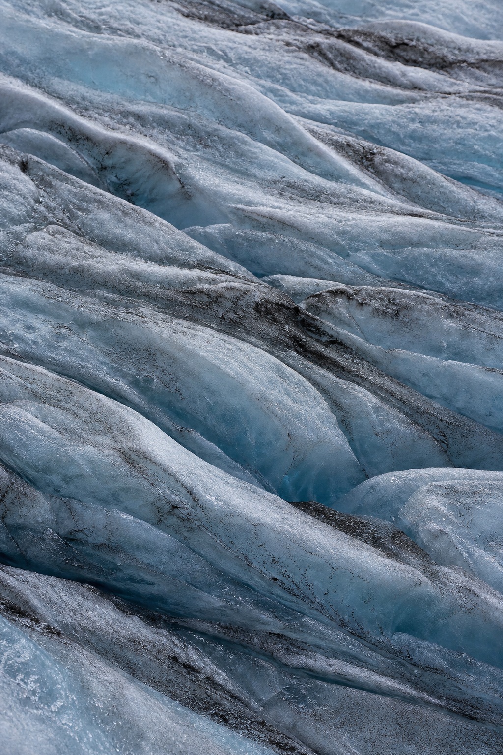 Blue glacial ice with shallow crevasse folds and textured frozen ridges