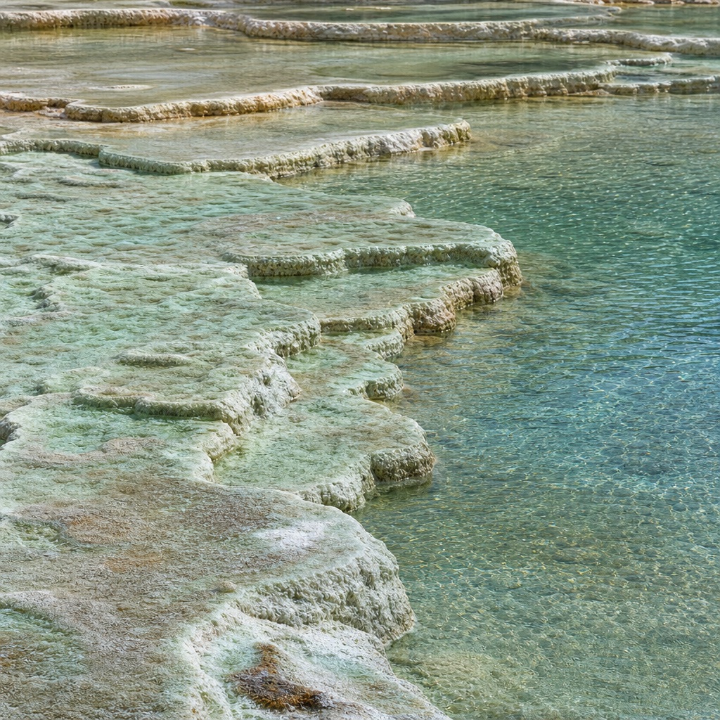 Layered seafoam-colored mineral ledges beside a clear turquoise salt flat