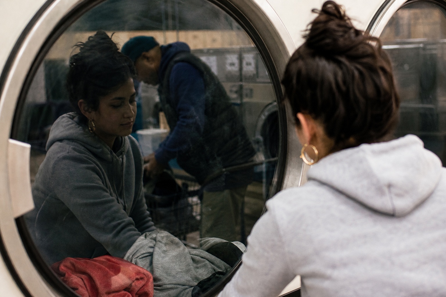 Two people seen through a laundromat window, with a reflected face in the glass.