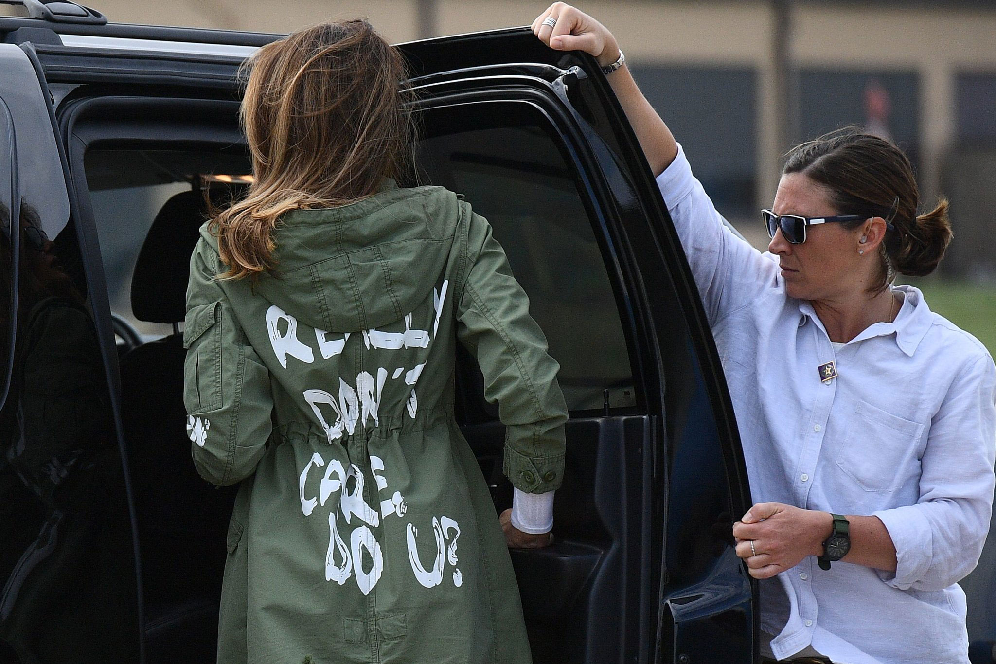 Woman helping a person wearing a graffiti-covered jacket beside a vehicle.