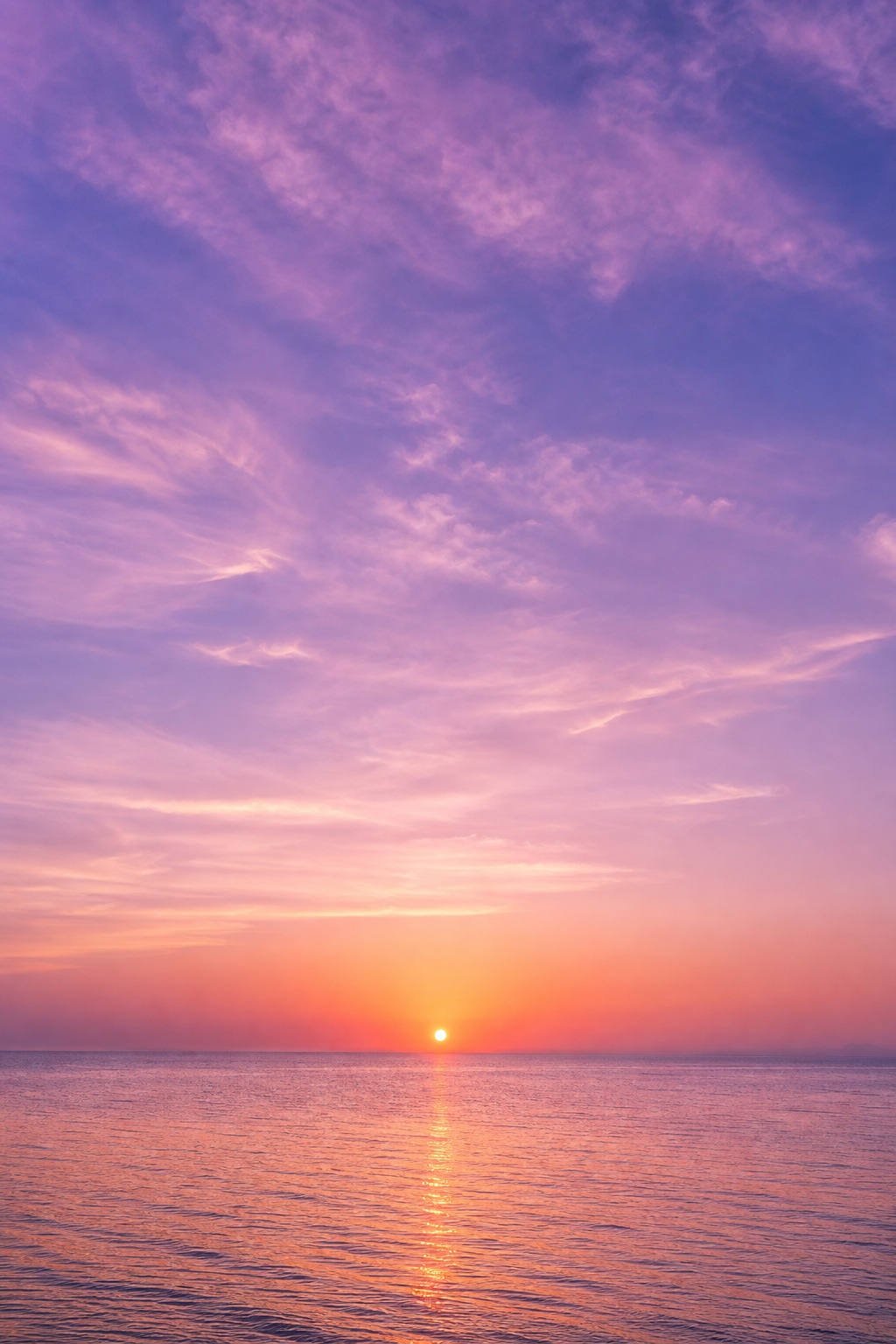 Vertical lavender sky over a calm ocean at sunset with the sun near the horizon.