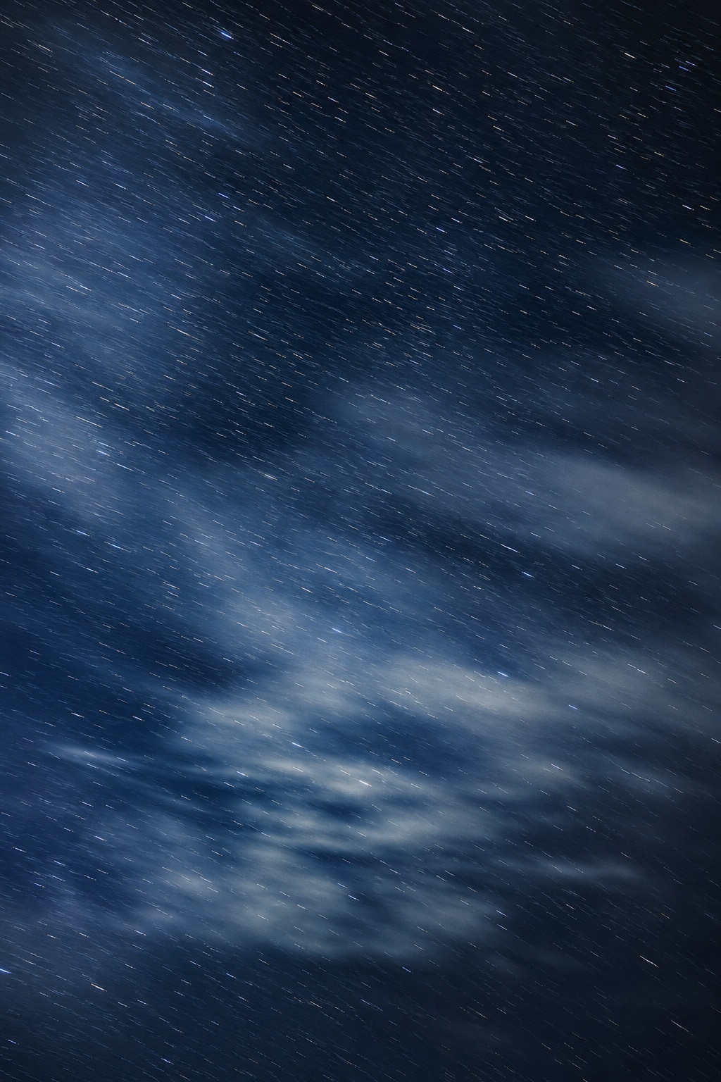 Silver blue night sky with long-exposure star streaks and soft clouds