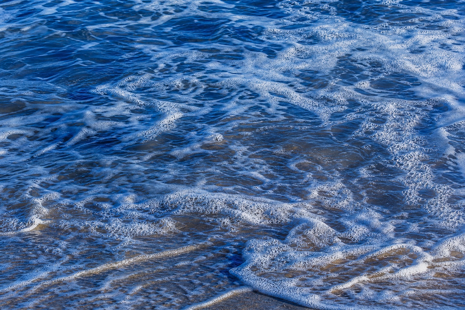 Blue ocean water with white foam ripples along the shoreline