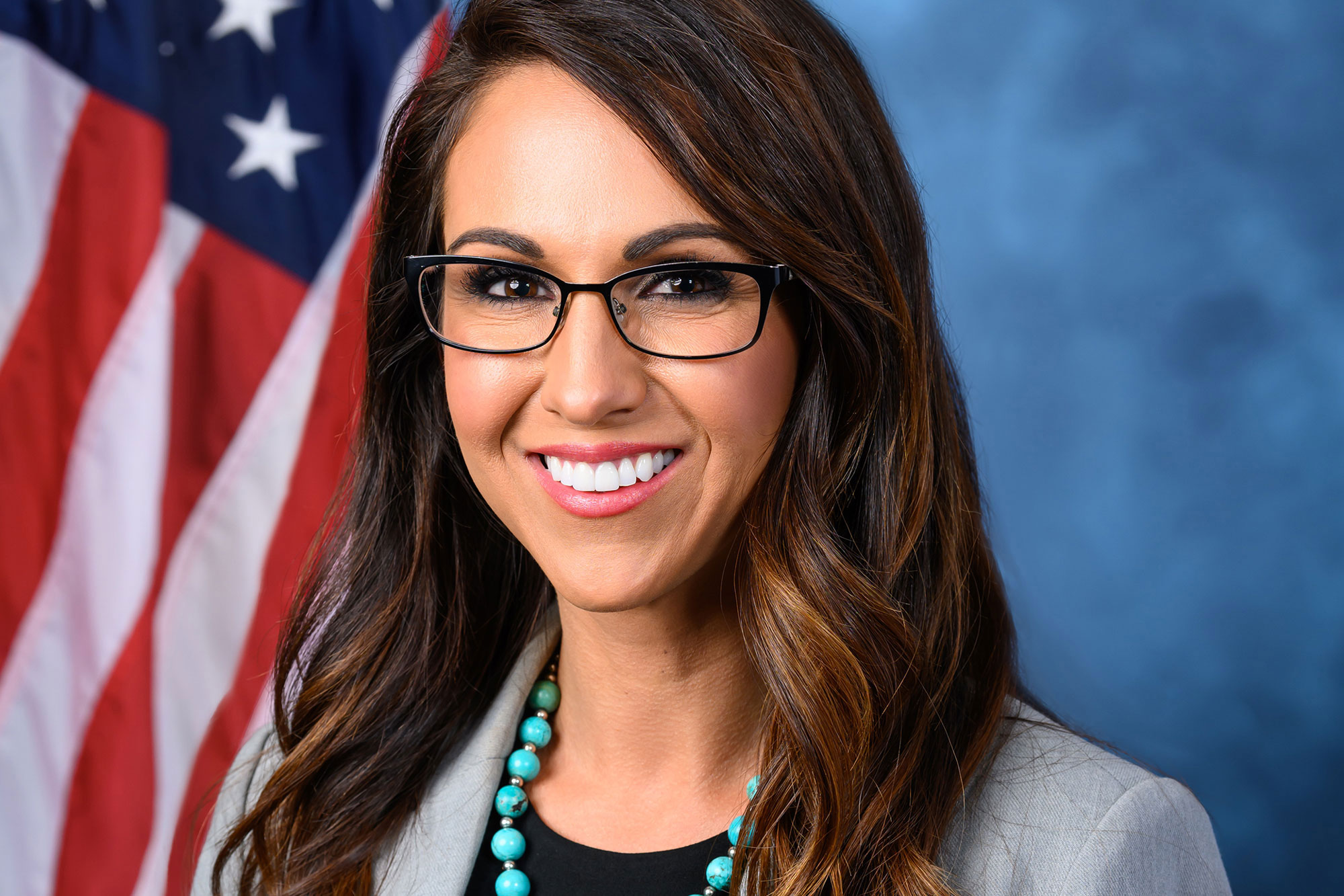 Smiling woman in glasses posed in front of a blue backdrop and American flag
