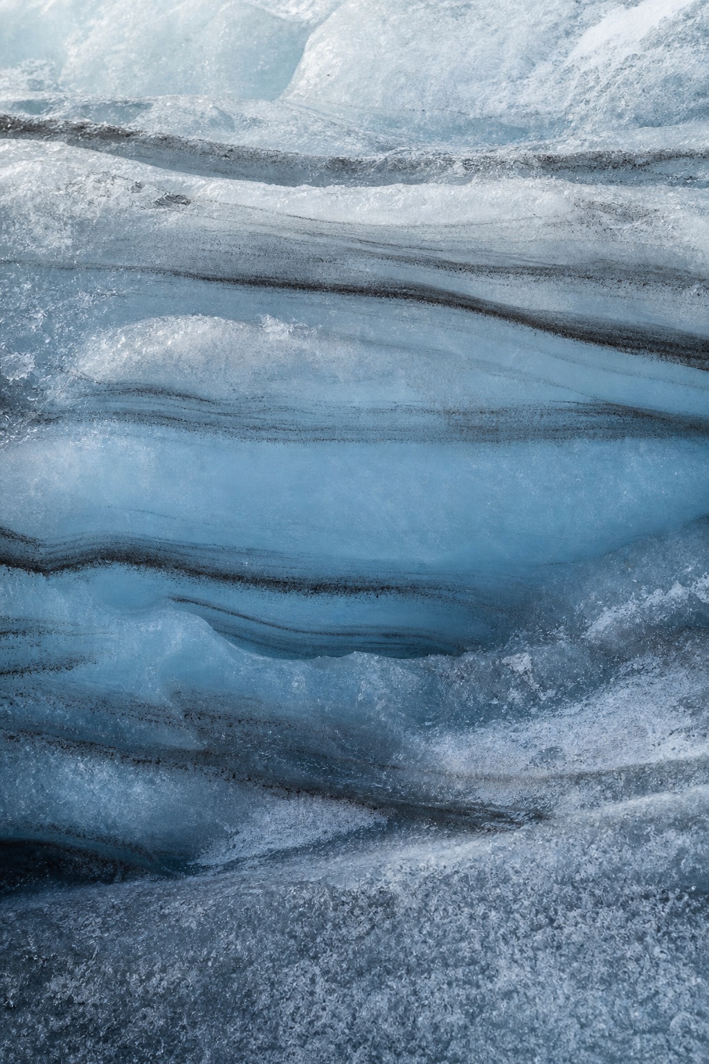 Blue glacier ice with layered crevasse bands and frosty sediment textures
