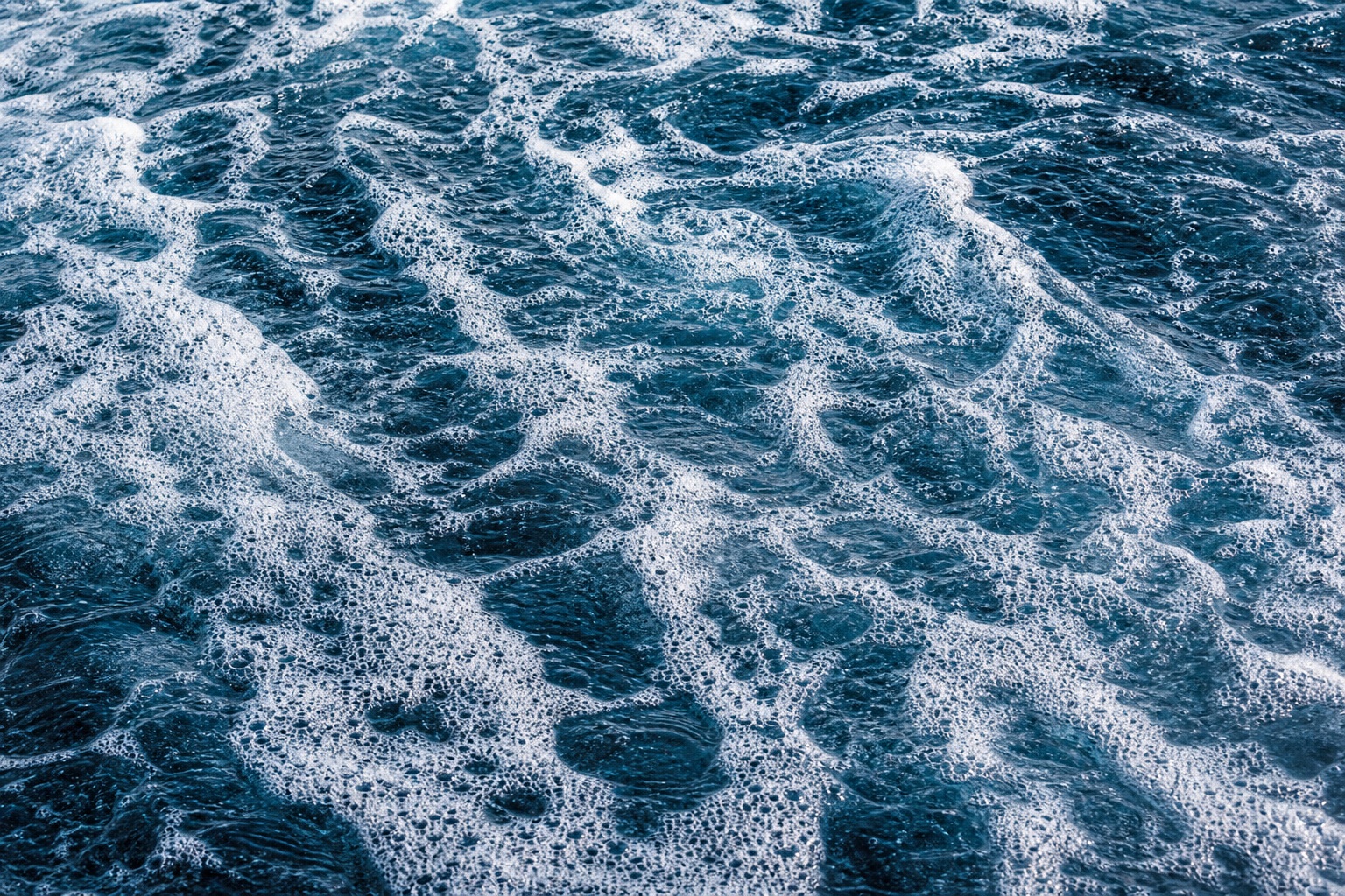 Blue ocean water covered with foamy wave patterns and shoreline texture