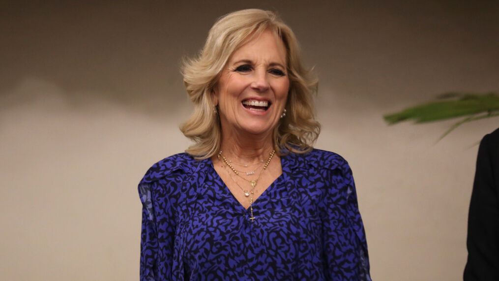 Smiling blonde woman in a blue patterned blouse against a neutral background.