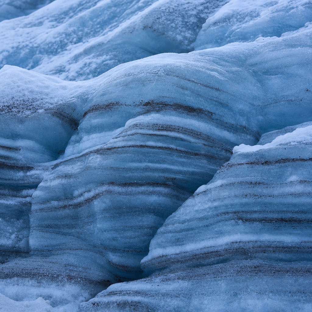 Blue glacier crevasse with layered sediment bands and icy mountain texture