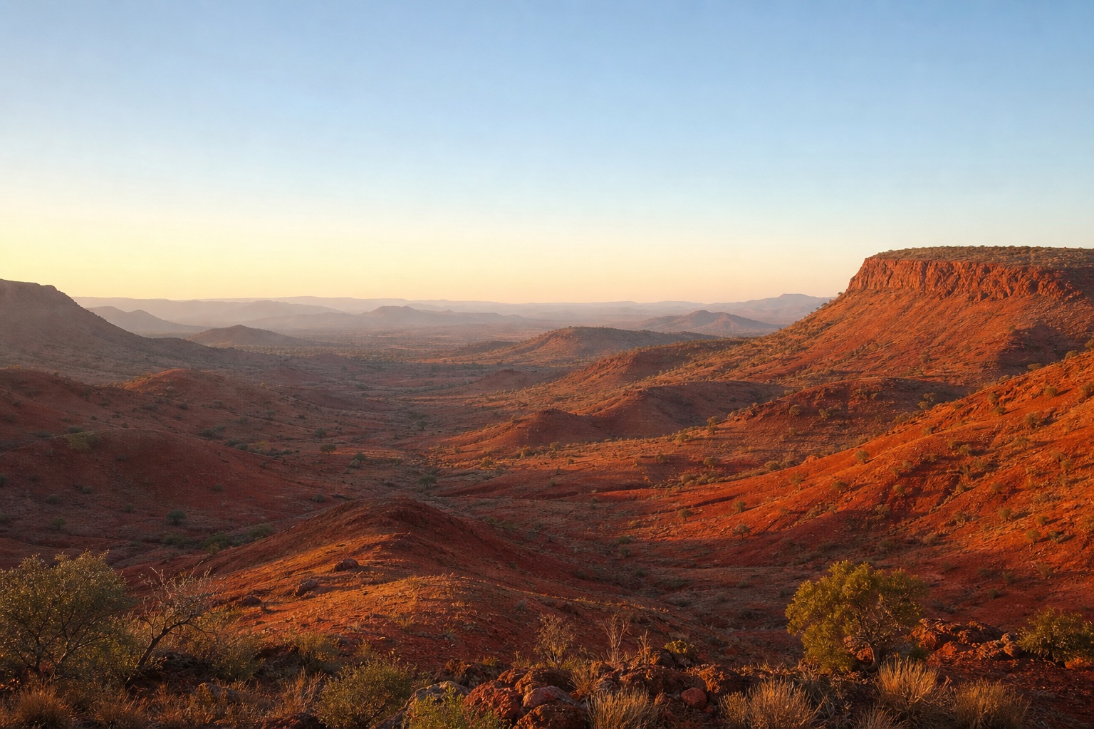 Sunrise over a red earth valley with layered hills and distant mountains