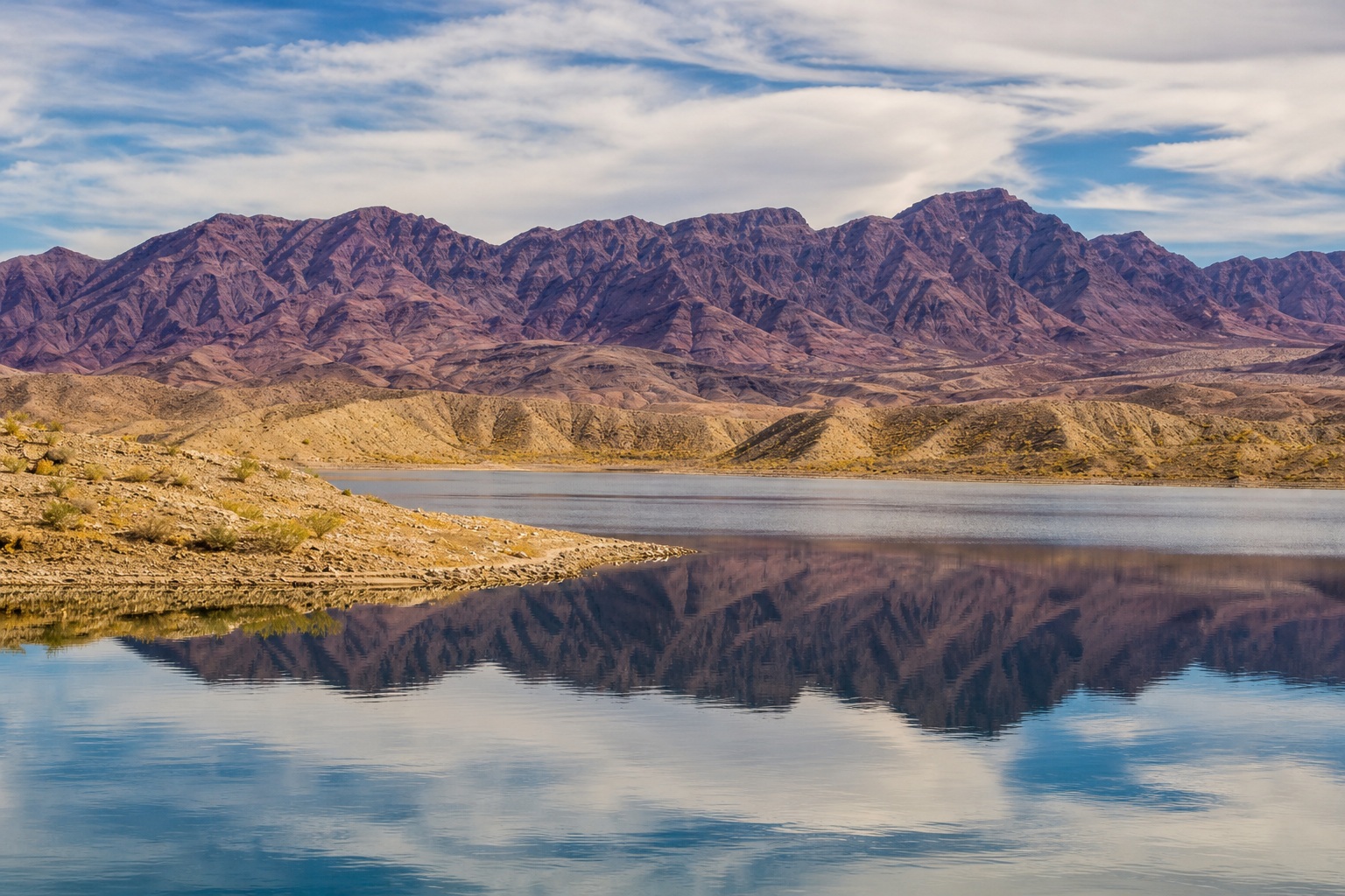 Mountain range reflected in a calm high desert reservoir under a clear sky.