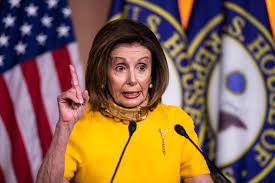 Nancy Pelosi speaking at a podium with a flag and seal in the background.