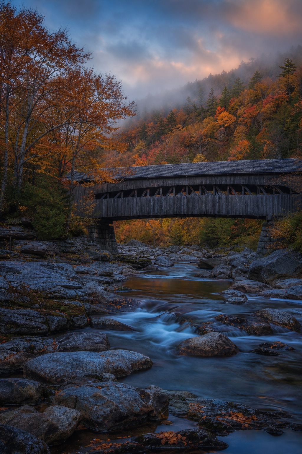 Covered bridge over a rocky river with autumn trees and cool twilight sky