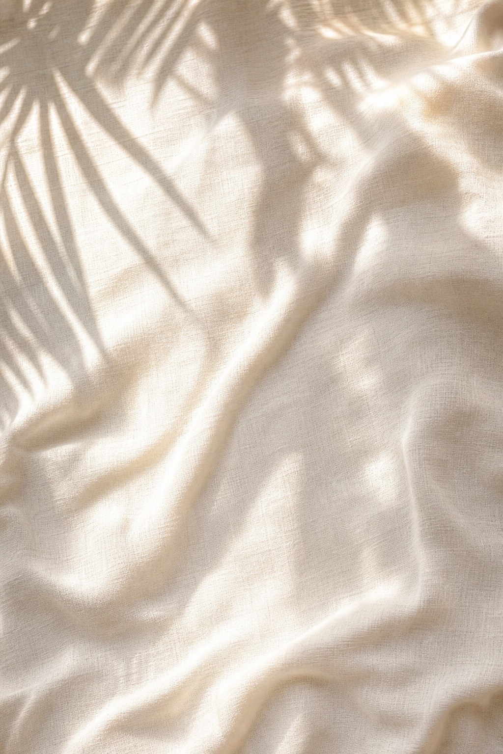 Sunlit linen fabric with soft palm leaf shadows across the surface