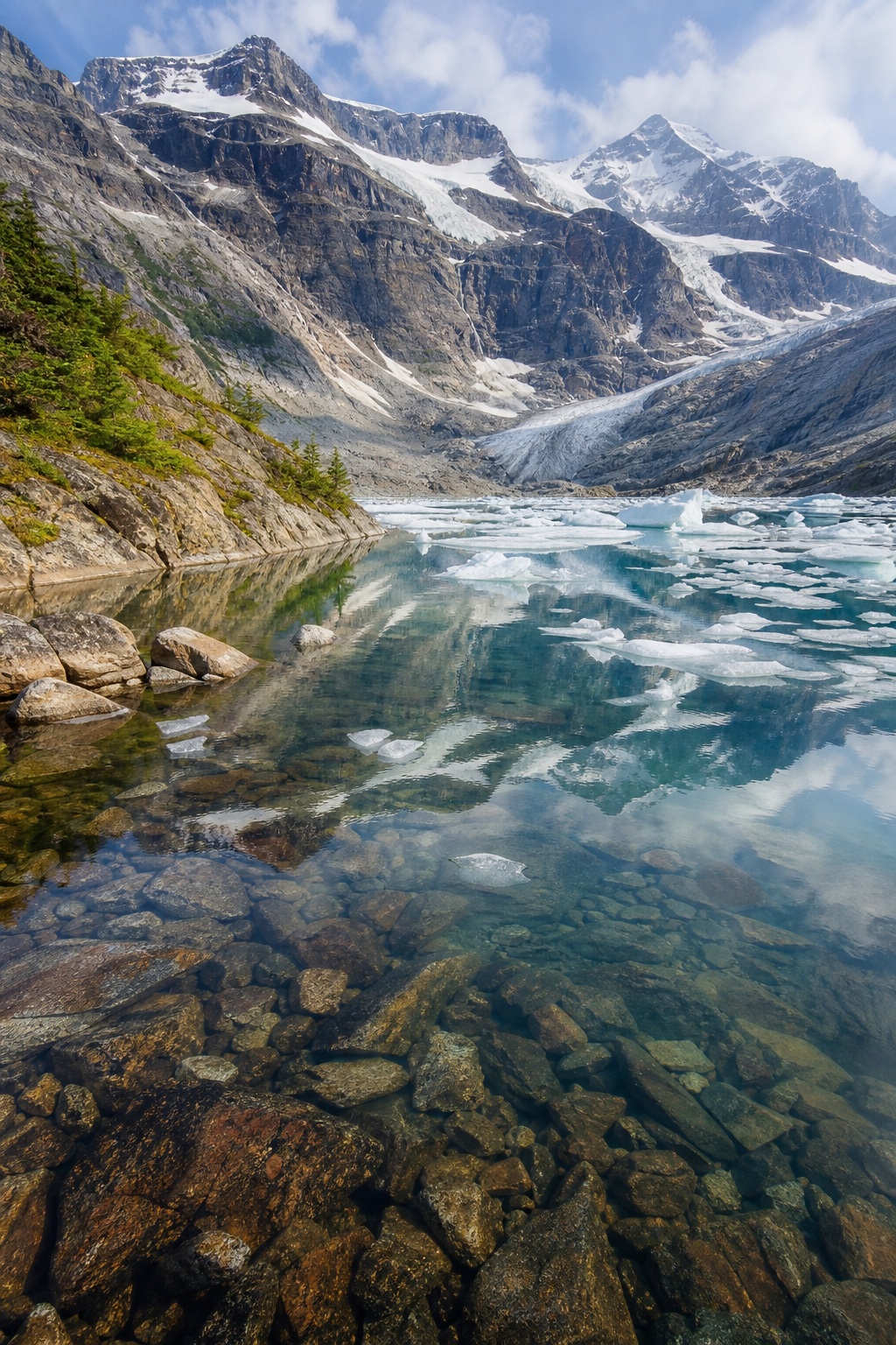 Glacier pond reflecting mountains and clouds with rocky shoreline and clear water