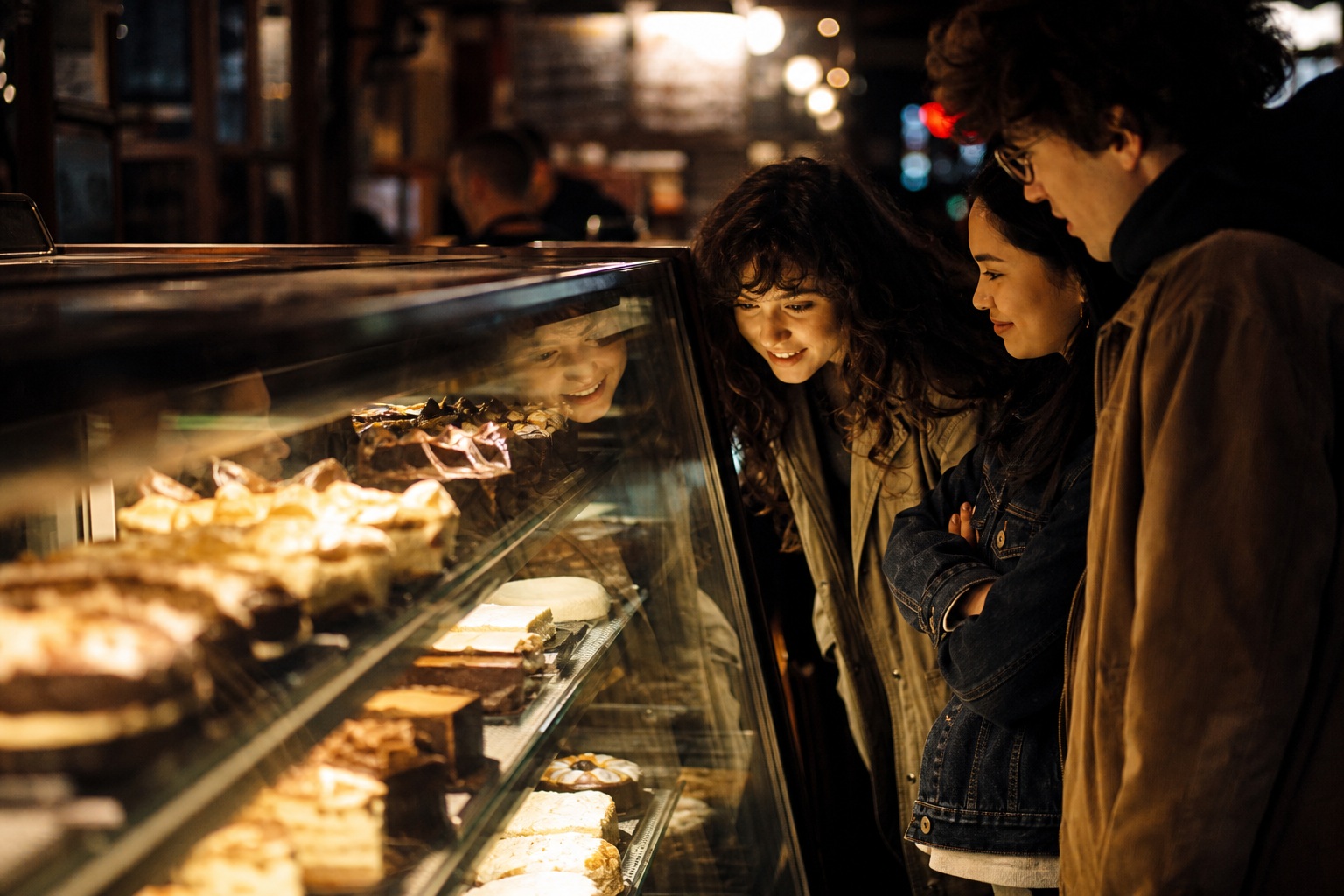 Candid people standing beside a glowing dessert case in a late-night diner