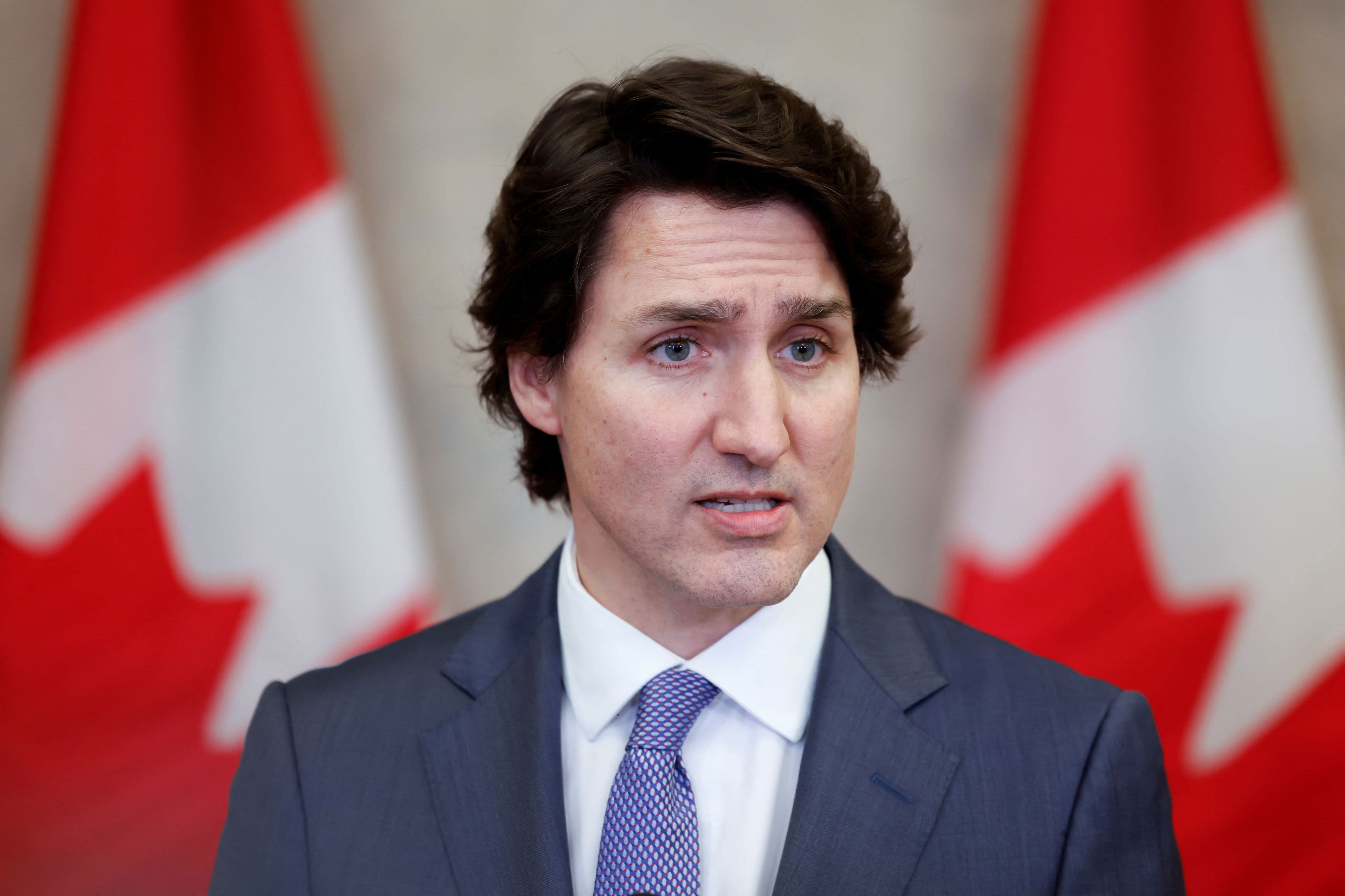 Formal portrait of Justin Trudeau standing before Canadian flags