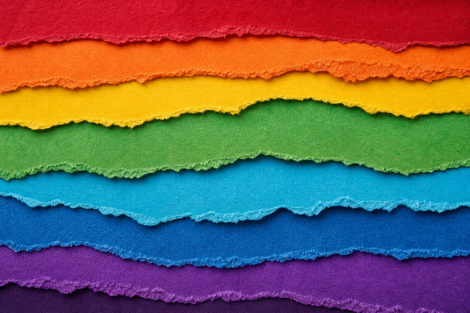Layered rainbow torn paper strips on a dark textured background.