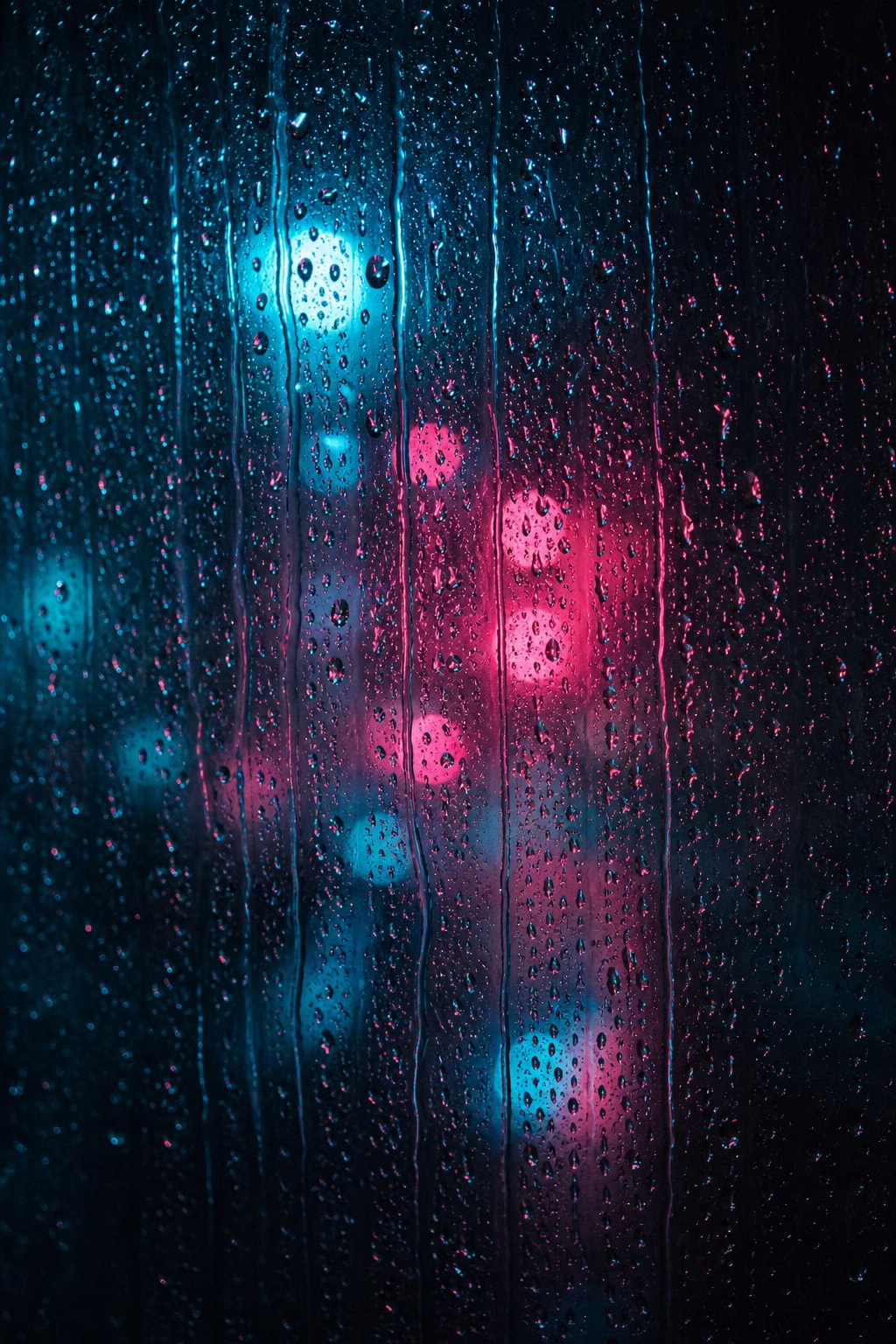 Blue and pink neon bokeh blurred behind rain droplets on a dark window.