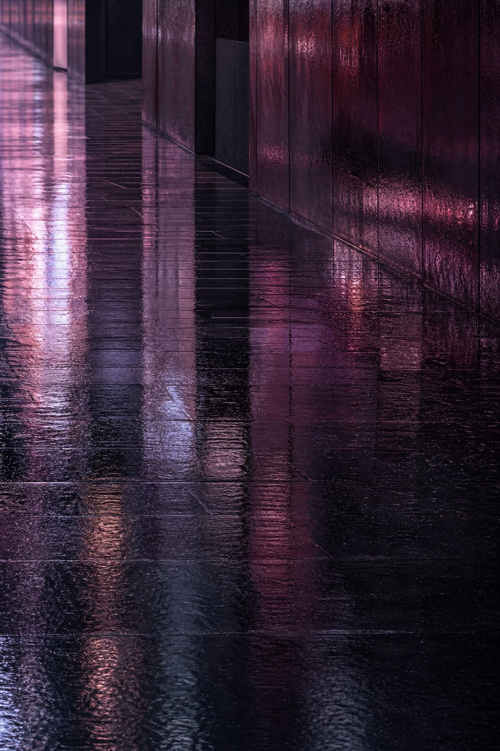 Shimmering wet pavement reflecting plum and pink city lights at night