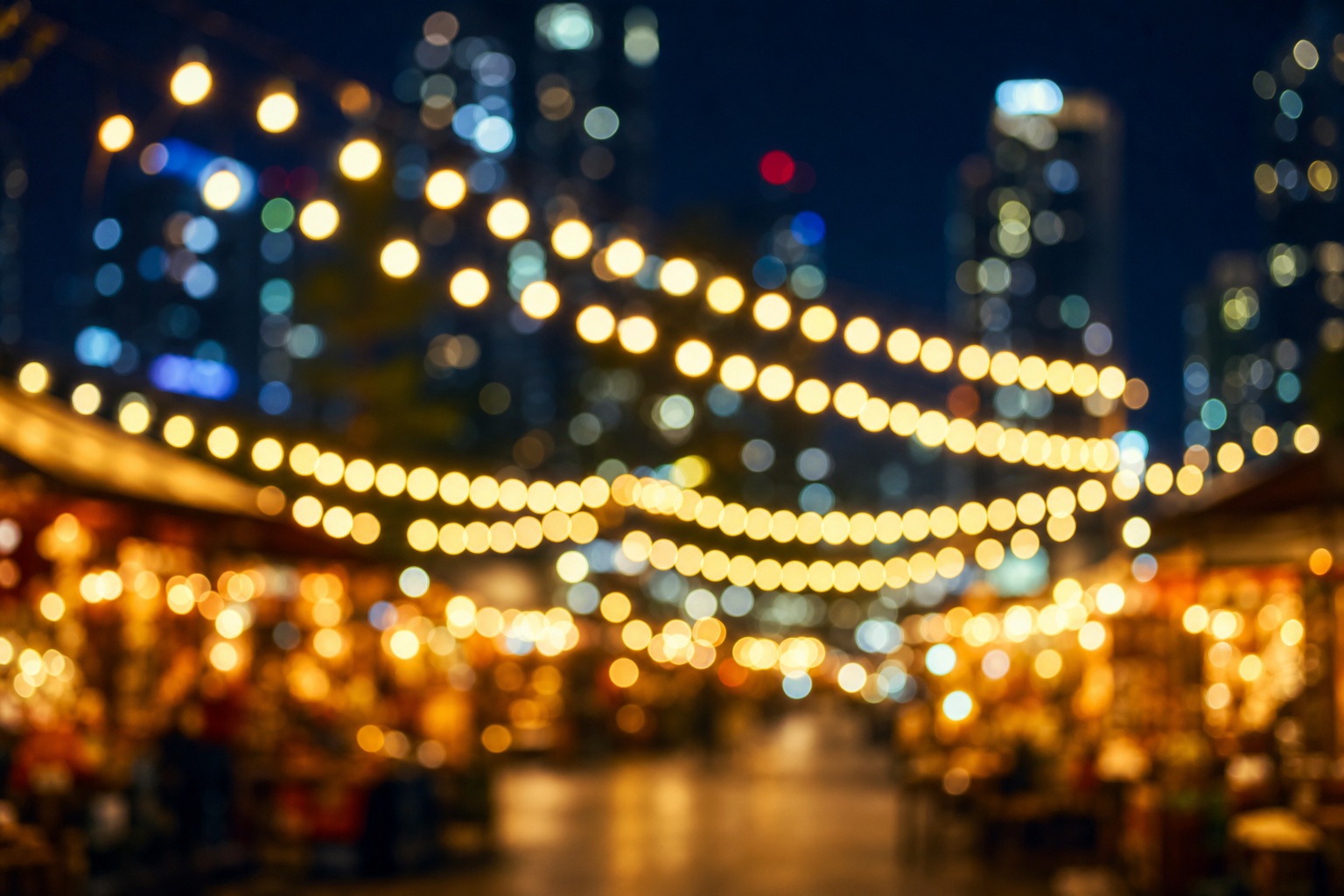 Blurred night market lights and city bokeh with warm glowing strings of lights.