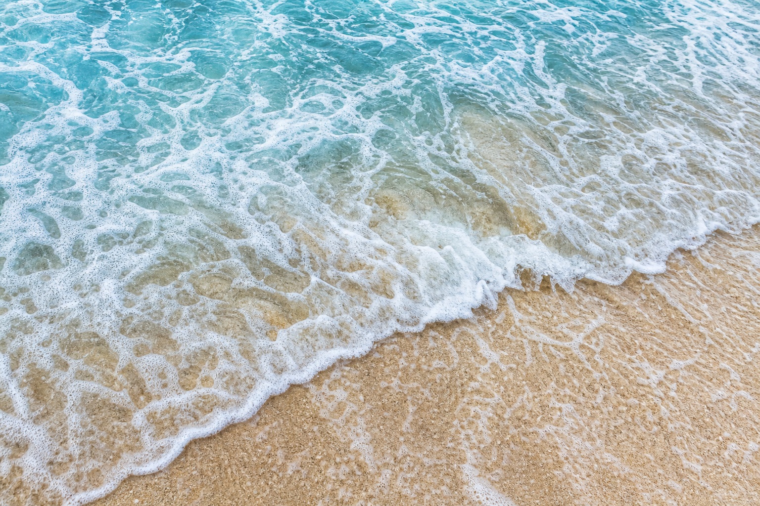 Foamy ocean waves washing over a sandy shoreline from above