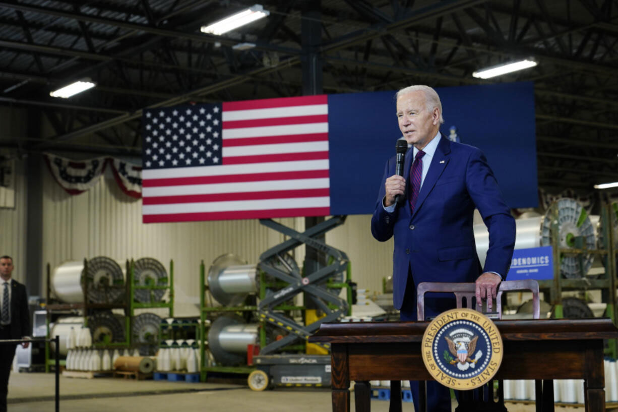 President Biden speaking at a podium beside a large U.S. flag in an indoor hangar