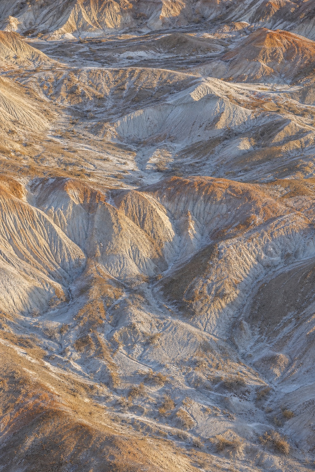 Eroded badlands hills with layered mineral gullies in cool winter sunlight