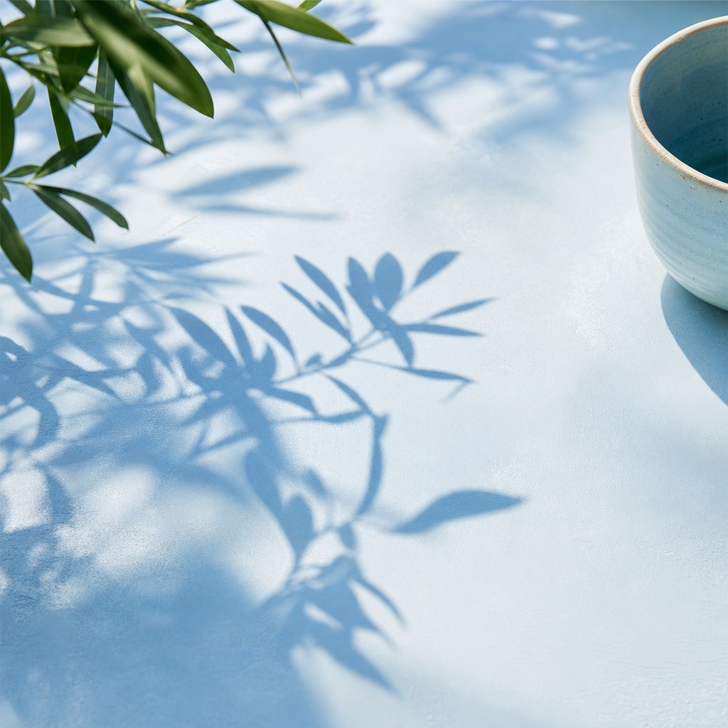 Pale blue desk surface with plant shadows and a cup in the corner